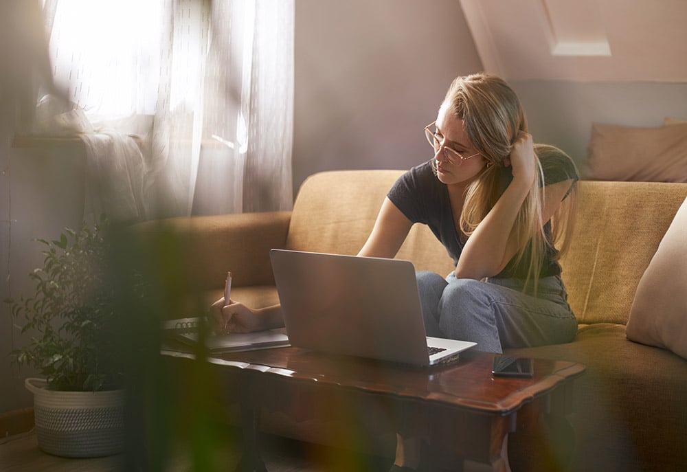 Woman sitting on a couch using a laptop and taking notes